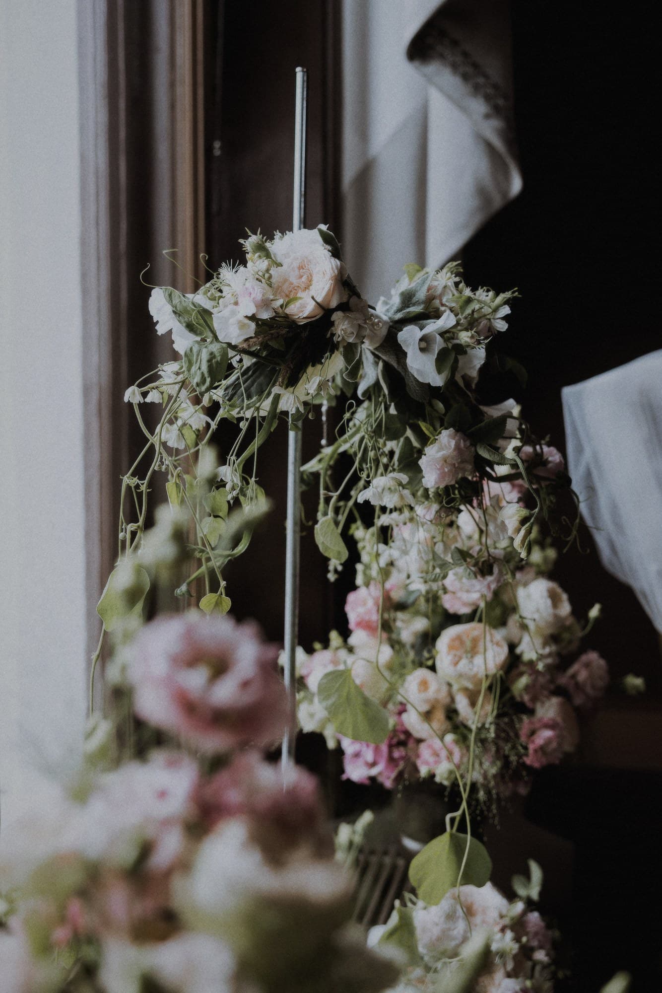 Ranka av rosor och lisianthus vid ett fönster med tungt draperi